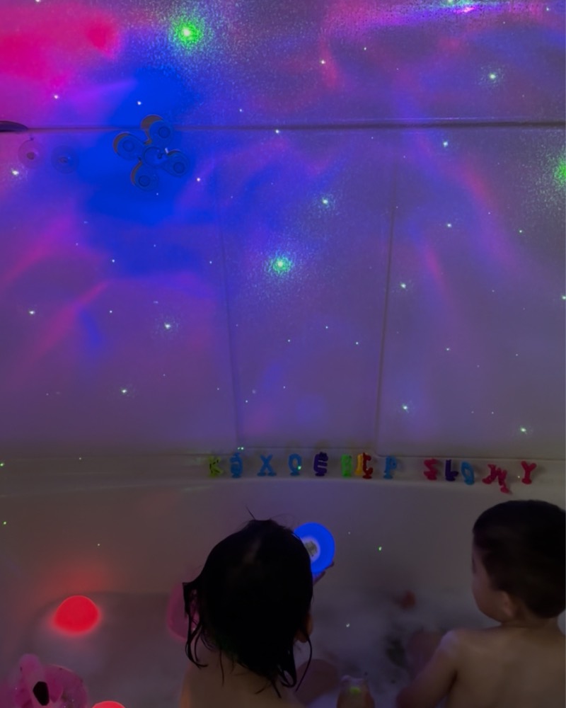 Two children playing with foam letters in the bath under starry lights